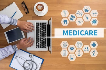 Person sitting at a table on their laptop with a notebook and coffee, Medicare and related icons in the open space on the table